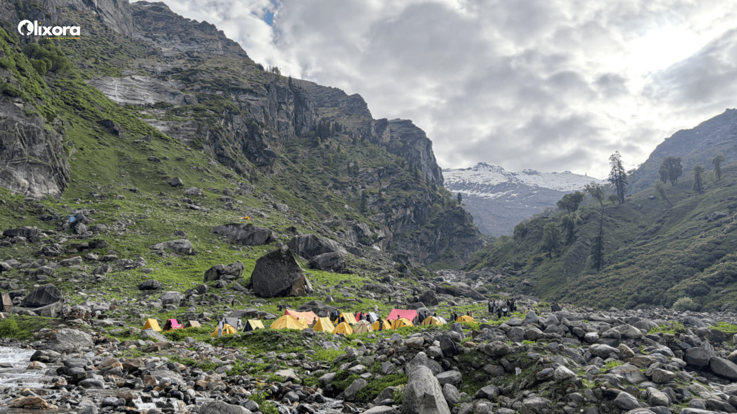 A sweeping panoramic view of the lush green Jobra forest contrasting with the distant snow-capped peaks of the Hampta Pass trail
