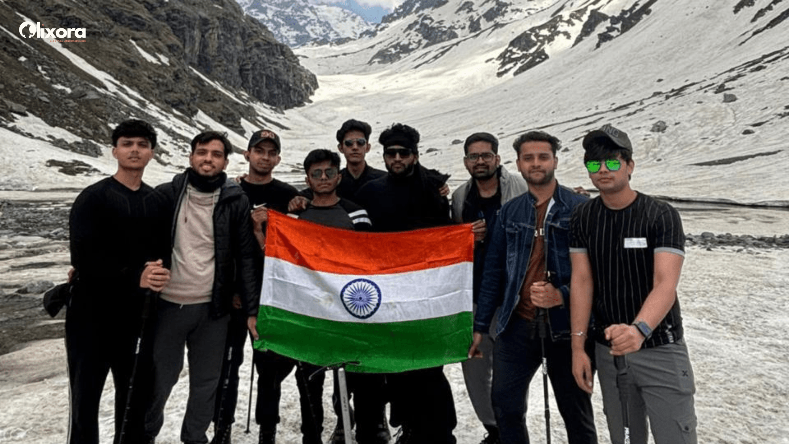 A happy group of Olixora trekkers holding Indian Flag at the windy summit of Hampta Pass