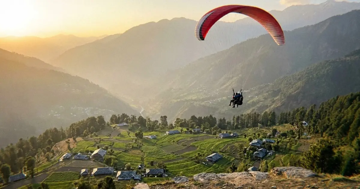 A tandem paraglider flying above a terraced valley in Himachal Pradesh