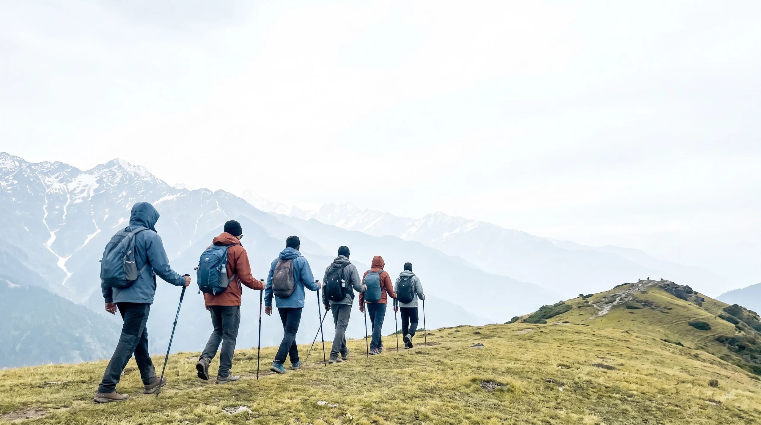 Trekkers walking single file along a Himalayan ridge trail with snow-capped peaks behind